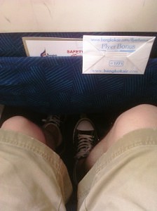 a person's legs and a paper in the back of a seat